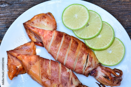 Grilled squid with lemon on white plate on wood table,sea food of Thailand