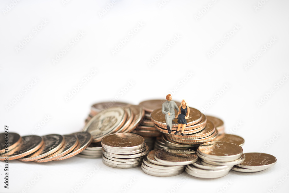 Miniature people: Small couple figures in love sitting on stack of coin in front of house. Money, Love and Valentine's day concepts. Miniature people: Small couple figures in love sitting on stack of coin in front of house. Money, Love and Valentine's day concepts.