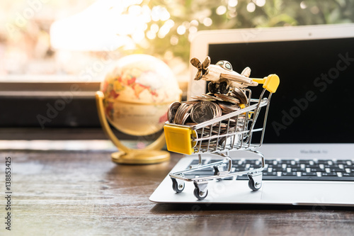 Small shopping cart filled with coins and miniature airplane on laptop using as business online concept.