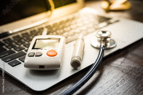 Technology and medicine - Silver stethoscope and blood glucose meter over laptop keyboard. Concept of healthcare medical and check up, diabetes, glycemia.