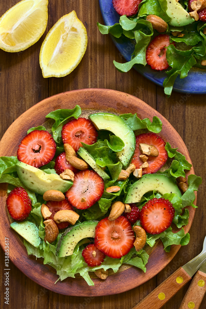 Strawberry, avocado, lettuce salad with cashew nuts on plate, photographed overhead on dark wood with natural light Strawberry, avocado, lettuce salad with cashew nuts on plate, photographed overhead on dark wood with natural light