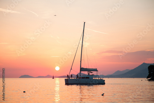 Yacht is sailing with people on background of sunset, sea, mountains, sky, sun. © Marina April