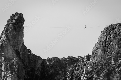 Person tight rope walking across cliff peaks, black and white, low angle view  photo