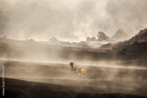 Tourists walking among steaming lava fields with volcano slope in background