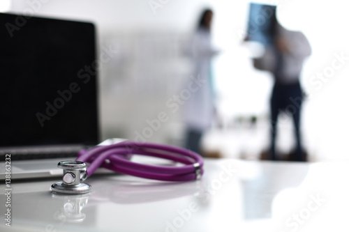 Laptop and stethoscope on the desk , doctors standing in the background photo