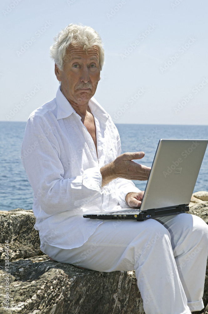 Mann, Senior mit Laptop im Sommerurlaub am Meer
