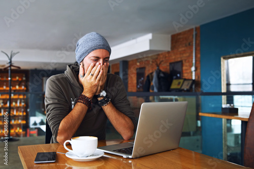 Worried shoked man with beard looking on laptop at cafe photo