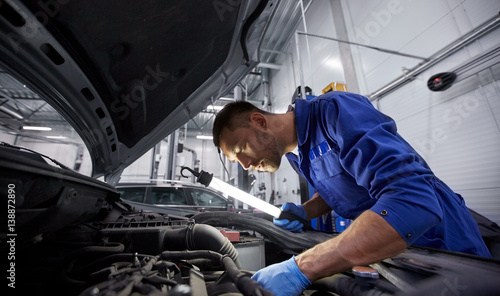 mechanic man with lamp repairing car at workshop