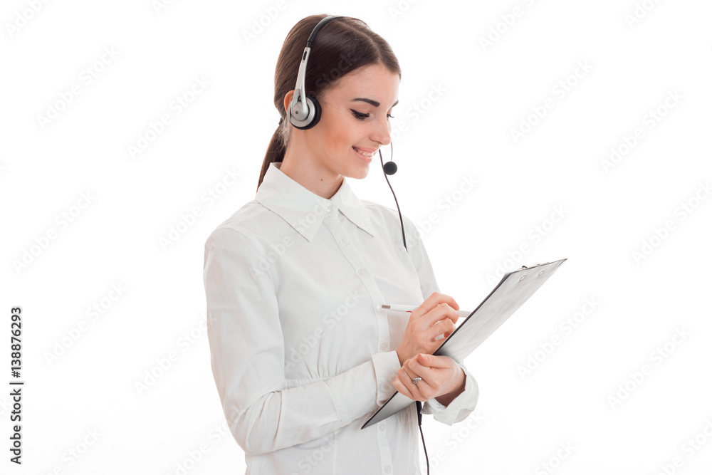 young girl in white shirt is worth turning sideways in headphones and writes something on paper young girl in white shirt is worth turning sideways in headphones and writes something on paper