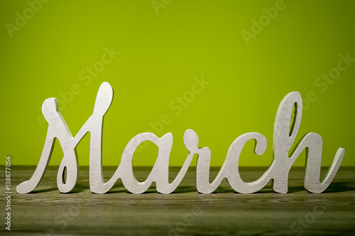 Close Up March word carved out of wood on green background. Spring beginning concept photo