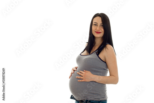 young pregnant girl with dark hair touching her big belly and looking at the camera isolated on white background