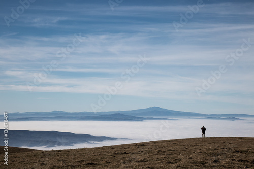 A man in a mountains scenery, with fog and big blue sky