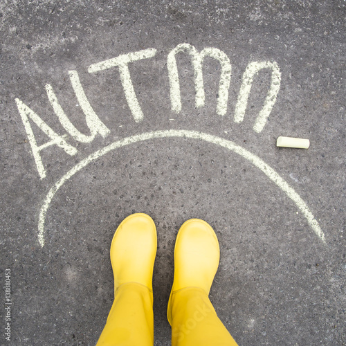 written on the pavement the word autumn. near yellow rubber boots