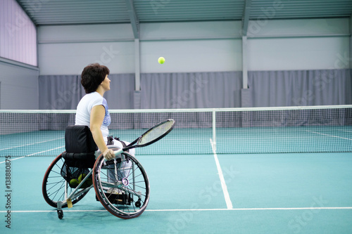 Disabled mature woman on wheelchair playing tennis on tennis court. © Nejron Photo