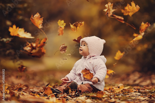 Маленький ребенок сидит в осеннем лесу и бросает желтые листья