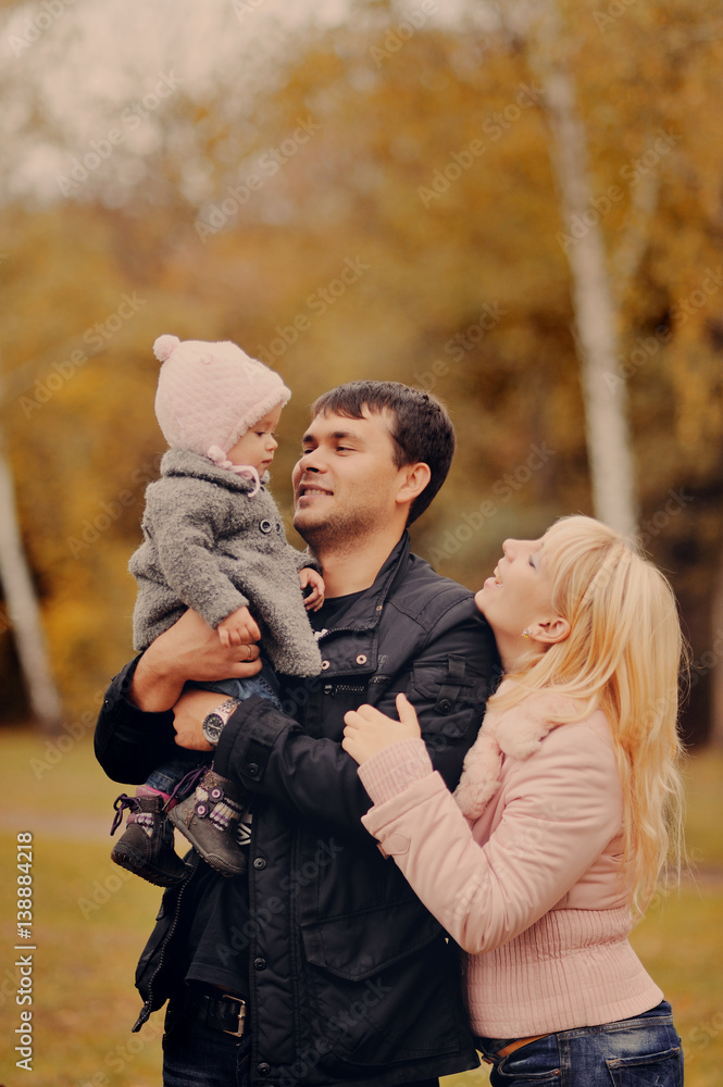 Fototapeta premium Молодые родители держат на руках маленькую дочь в осеннем парке