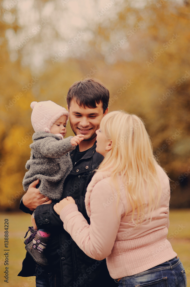 Молодые родители держат на руках маленькую дочь в осеннем парке Молодые родители держат на руках маленькую дочь в осеннем парке