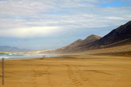 Beach Cofete and a couple walking along it on Fuerteventura, Spain.