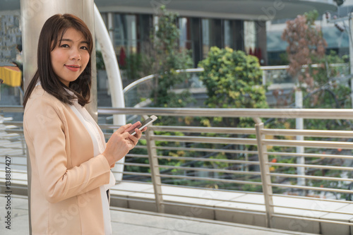 Beautiful girl holding a smart phone turned smiling happily in the city.Copy space on the right