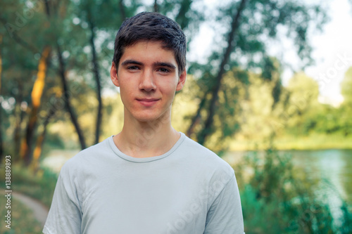 A young man with black hair smiling. Portrait of a gay in nature. Sunny sunset behind the man.