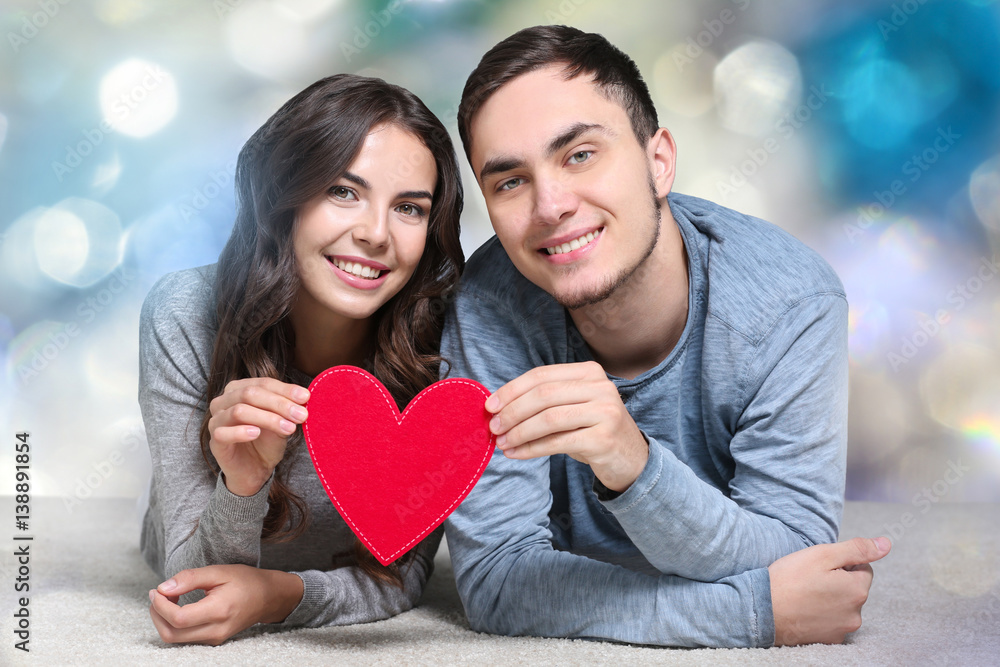 Beautiful young couple holding felt heart in hands on blurred background