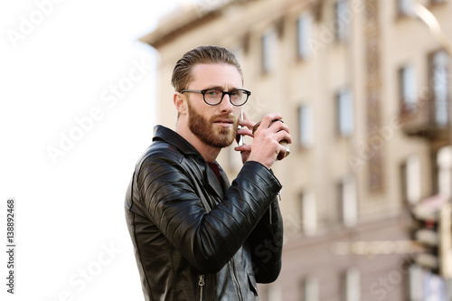 Young man with cup of coffee talking on phone outdoors