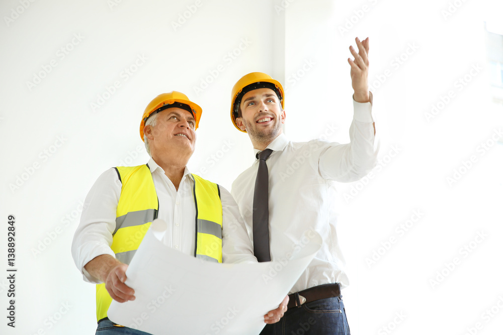 Handsome engineer and worker discussing plan of works while standing inside new building Handsome engineer and worker discussing plan of works while standing inside new building