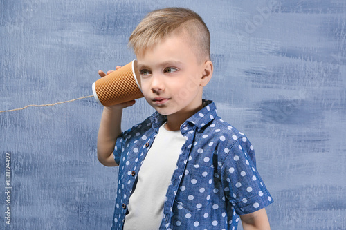 Cute little boy using plastic cup as telephone, on color background photo