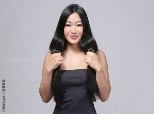 Beautiful Asian woman with long straight hair on light background