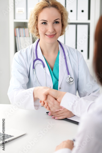 Happy blonde female doctor shaking hands with patient while speaking to her. Medicine, healthcare and help concept