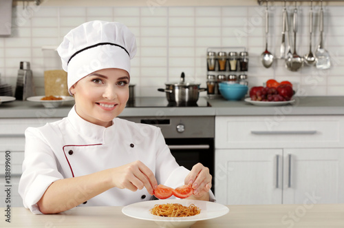 Young woman chef putting tomato slices on plate with pasta