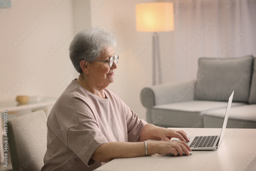 Elderly woman working on laptop in light room Elderly woman working on laptop in light room