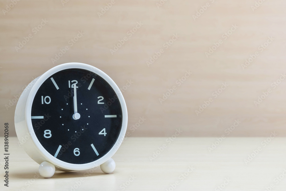 Closeup alarm clock for decorate in 12 o'clock on brown wood desk and wall textured background with copy space Closeup alarm clock for decorate in 12 o'clock on brown wood desk and wall textured background with copy space