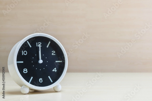 Closeup alarm clock for decorate in 12 o'clock on brown wood desk and wall textured background with copy space