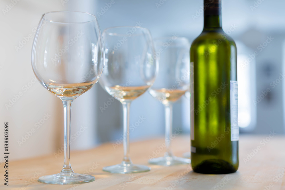 Three clear wine glasses and a bottle of chilled white wine on a wooden table

