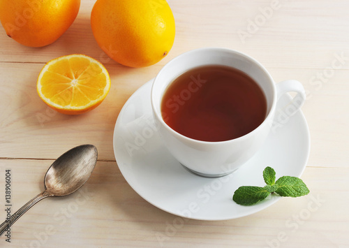 white mug with black tea, teaspoon, lemon and mint