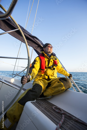Man Sitting While Holding Helm Of Yacht Against Sky