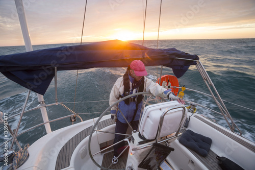 Man Standing At Helm Of Yacht Sailing In Sea During Sunset