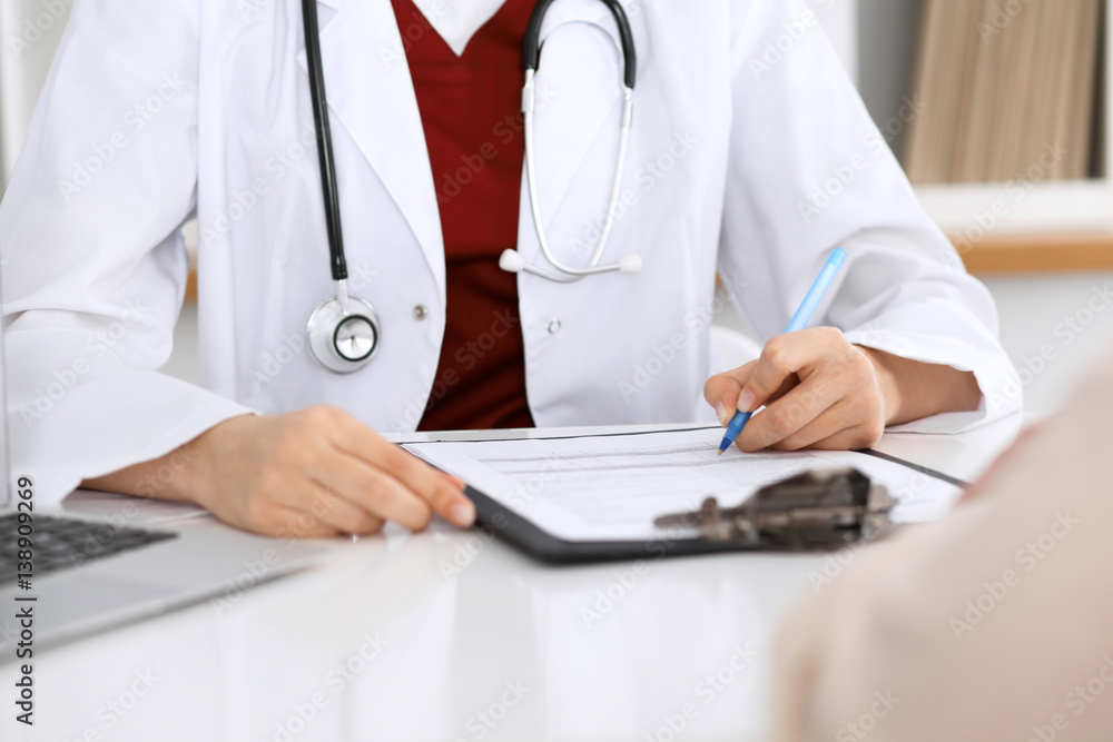 Close up of a female doctor filling up an application form while consulting patient. Medicine and health care concept Close up of a female doctor filling up an application form while consulting patient. Medicine and health care concept