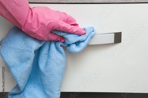 Hand in pink protective glove wiping wooden furniture with rag. Early spring cleaning or regular clean up. Maid cleans house.