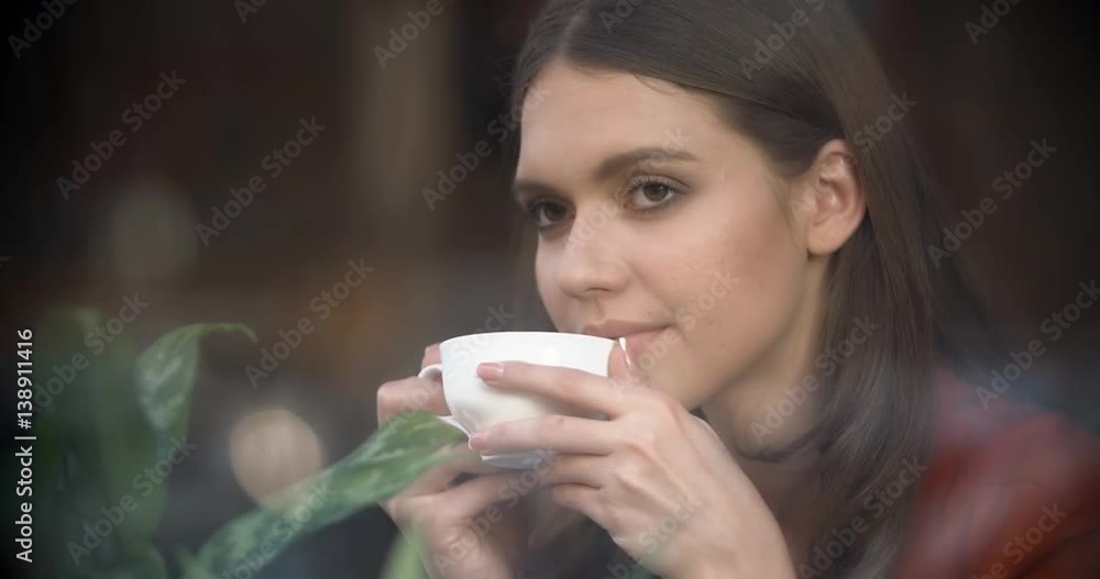 Girl with a cup of coffee in a cafe, dreamily watching the street life of the city, outside view