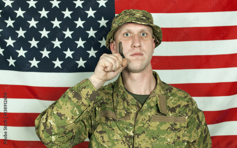 Young soldier with camouflage paint on cheek against of American flag. Portrait Young soldier with camouflage paint on cheek against of American flag. Portrait