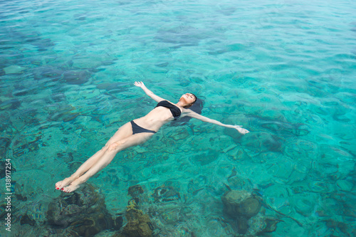 Beautiful young brunette woman in black swimsuit swims into clear azure water of caribbean sea
