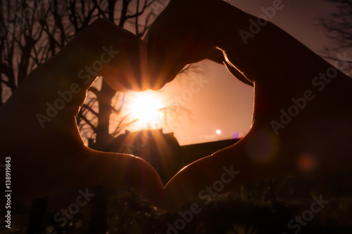 Heart shape made by fingers silhouette with sunset background