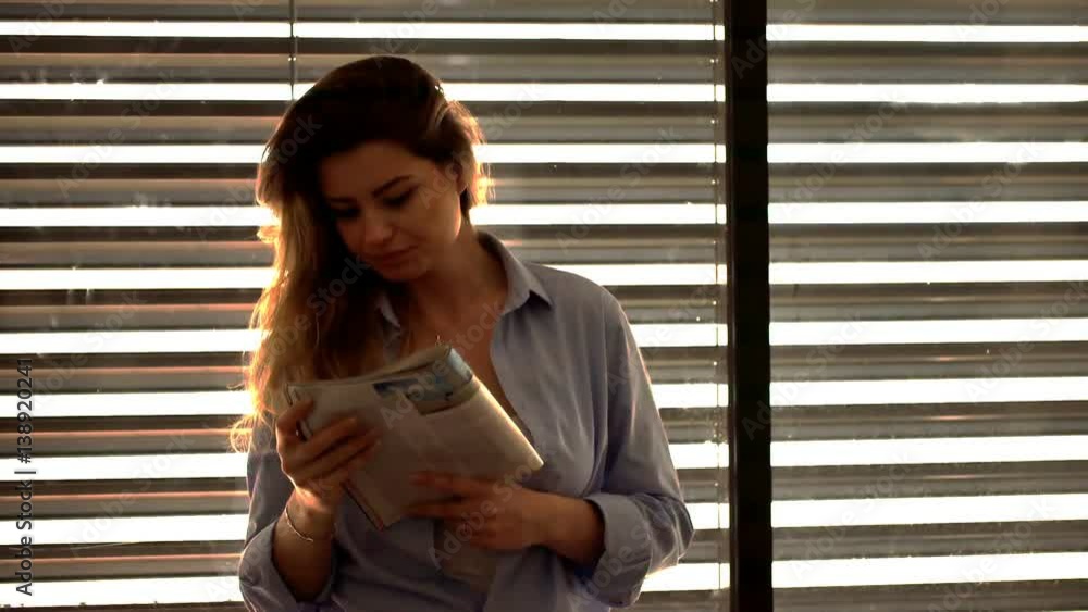 Attractive woman standing next to the window and reading magazine
Attractive woman standing next to the window and reading magazine