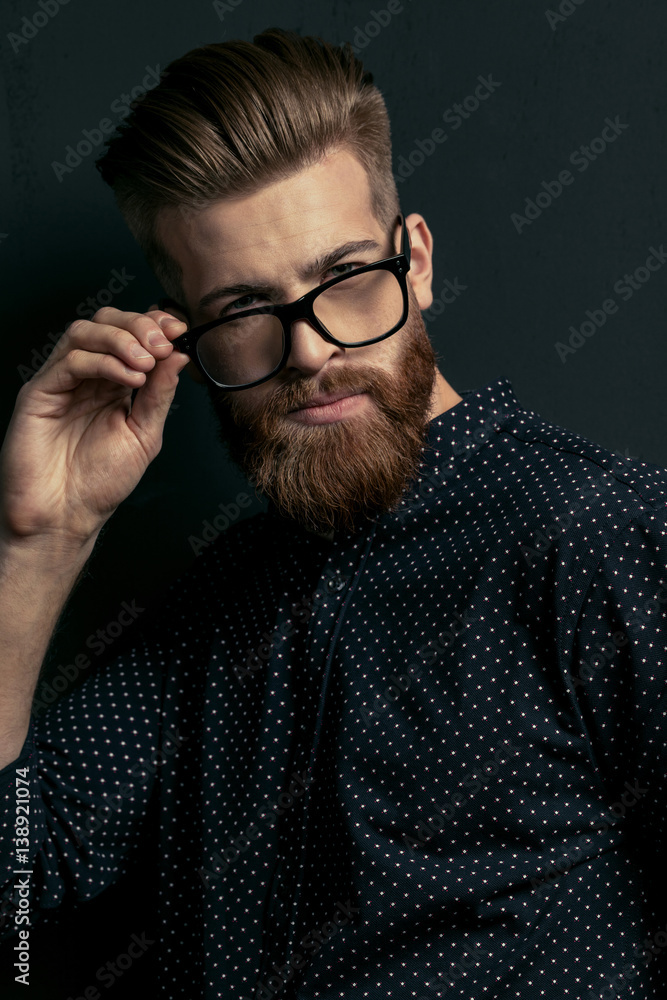Obraz premium Handsome bearded young man hipster adjusting eyeglasses and looking at camera