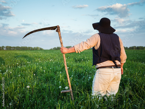 Farmer with a scythe on green field