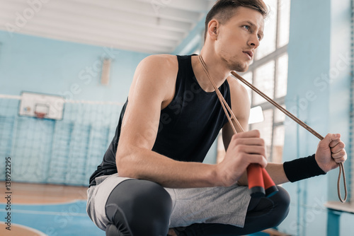 Pensive young sportsman crouching with skipping rope on neck in sports hall © LIGHTFIELD STUDIOS