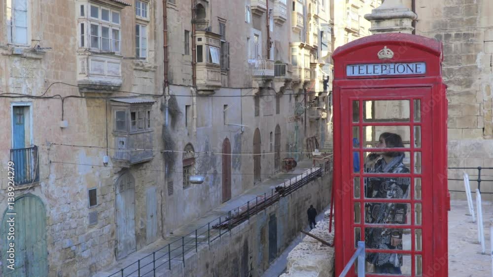 woman talking on the phone in a red telephone booth in a small village woman talking on the phone in a red telephone booth in a small village