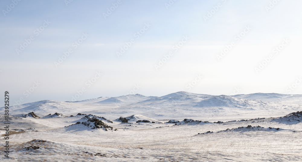Mountain winter landscape. with high hills Olkhon offers beautiful views of Lake Baikal, covered with ice. Snow-capped mountains on the horizon. Sunny day. Photo partially tinted.